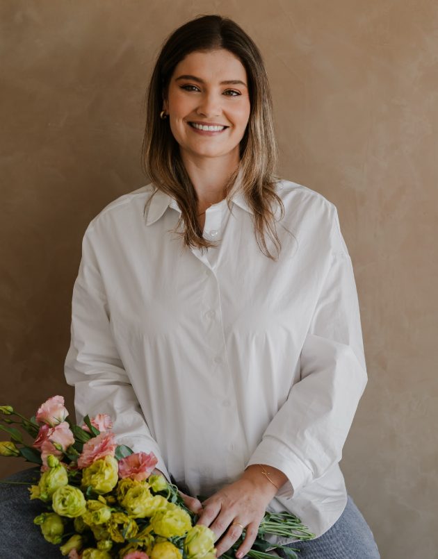Fabiane, a Fabi da Dream, sorrindo com um buquê de lisianthus rosa e verde no colo