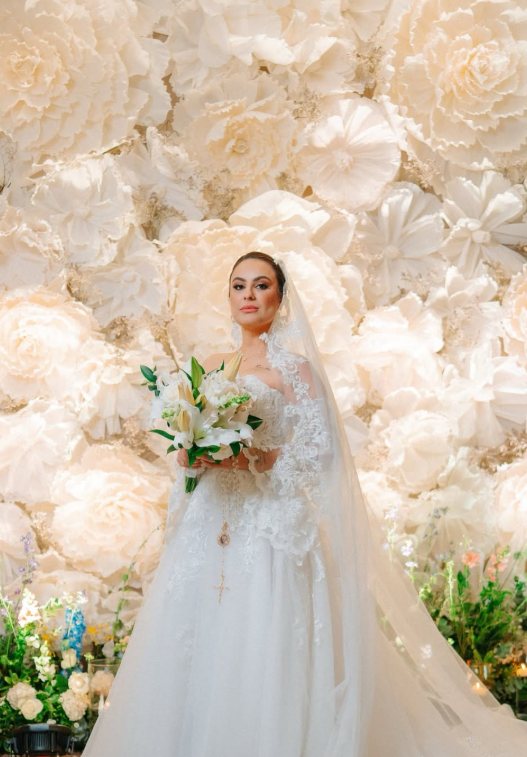 Noiva com buquê de lírios diante de um painel de flores gigantes brancas